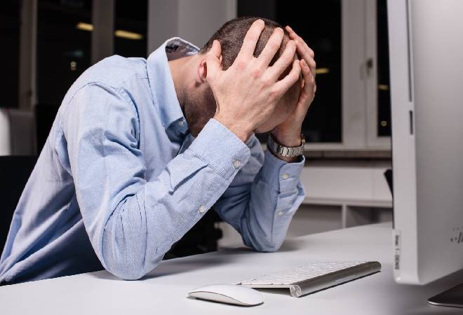 パソコンの前で項垂れる男性の姿。