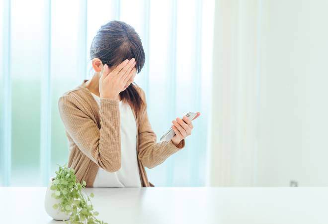 スマホ画面を見て目を覆う女性の姿。